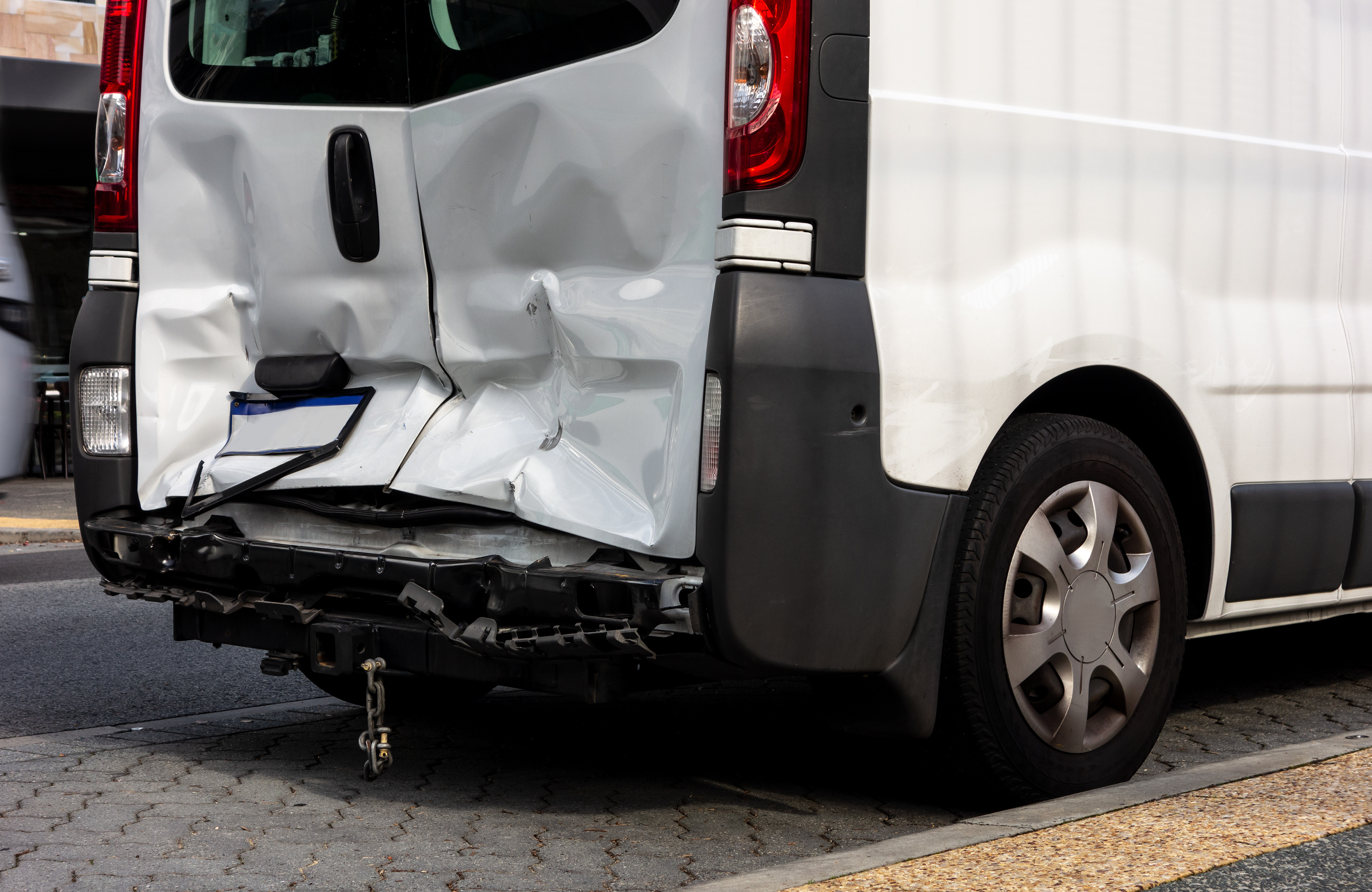 White van with severe rear damage, including crushed doors and bent bumper, parked on a street.